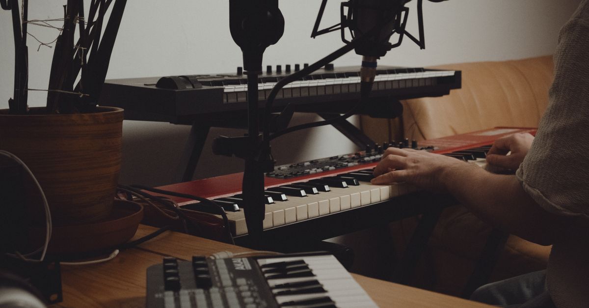 Person playing keyboard in a home music studio with recording equipment.
